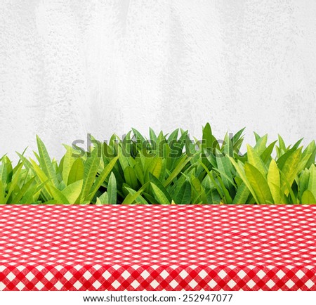 Empty table with red checked tablecloth over tree leaves and cement wall background, product display