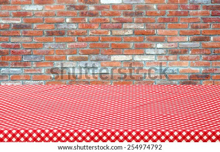 Empty table covered with red checked tablecloth over brick wall background, product display