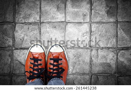 Feet in leather sneaker on pavement background, top view