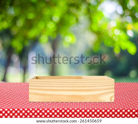 Wooden storage box on table with red tablecloth and blur green leaves bokeh background, for product display montage