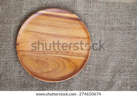 Empty round wooden plate on sack cloth background, food display montage
