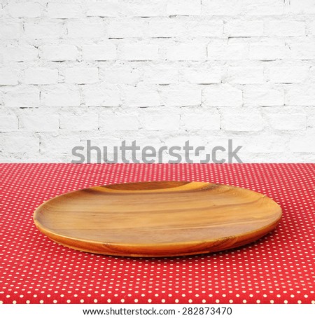 Empty round wooden tray on red polka dot tablecloth over white brick wall background, for product display montage
