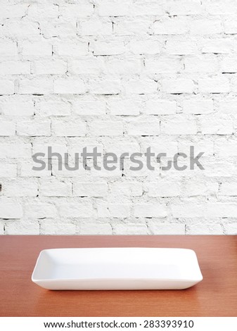 Empty plate on wood table over white brick wall background, template