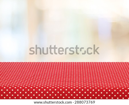 Empty table with red polka dot tablecloth over abstract blur bokeh background, for product display montage