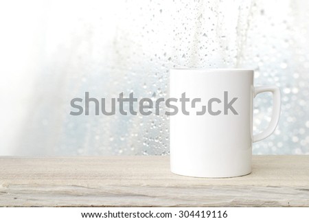 Coffee cup on wood table over blurred rain drop background