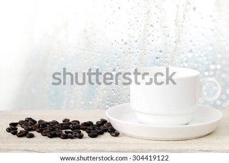 Coffee cup and beans on wood table over blurred rain drop background