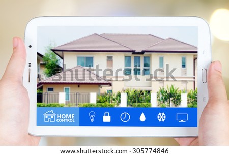 Hand holding tablet with smart home application on the screen over blurred house background, smart home concept