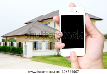 Hand holding white mobile smart phone over blurred house background, smart home concept, template, mock up