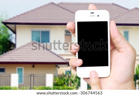 Hand holding white mobile smart phone blurred house background, smart home concept, template, mock up