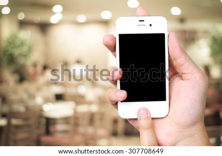Hand holding smartphone over blur restaurant background, restaurant reservation, food online, food delivery concept