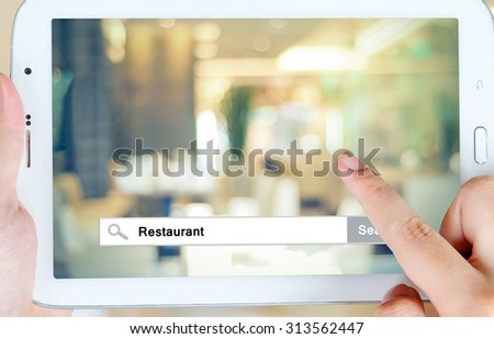 Hand holding tablet with restaurant word on search bar over blur restaurant background on screen, restaurant reservation, food online, food delivery concept