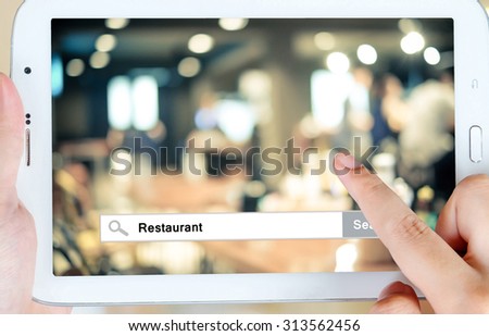 Hand holding tablet with restaurant word on search bar over blur restaurant background on screen, restaurant reservation, food online, food delivery concept