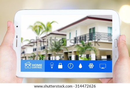Hand holding tablet with smart home application on the screen over blurred house background, smart home concept