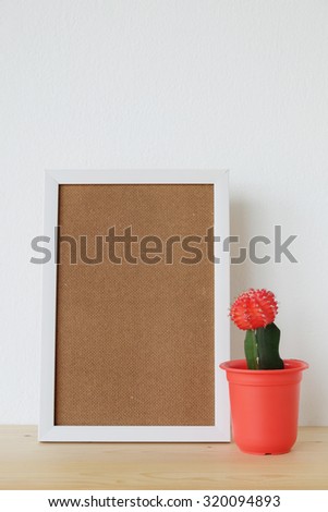 Blank white wooden frame and cactus on wood board over white cement wall background, template ,mock up