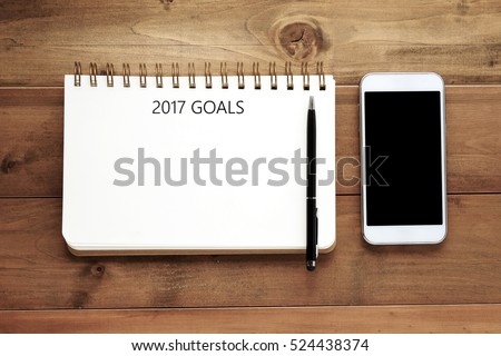 2017 goals word on blank notebook paper, pen and smart phone on wood background, financial concept, business strategy