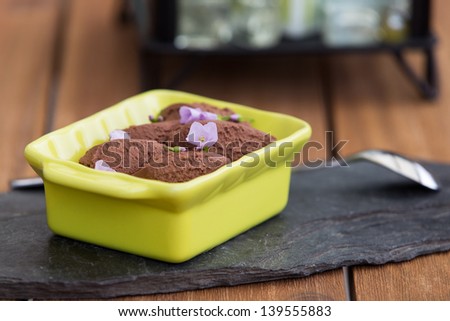 Chocolate mousse decorated with violets in green jar on stone slate