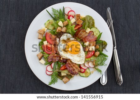Greek salad also called peasant salad, village salad or country salad. Composed with lettuce, cucumber, onion, radish, fried egg and bacon, cheese, tomatoes, parsley and croutons.