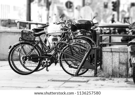 Some old bikes parked on the street in Milan city in Italy, in a black and white vintage photo.