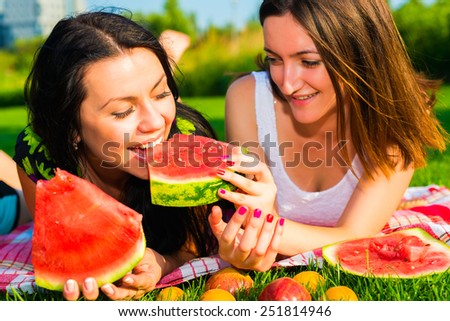 Two  young happy girlfriends picnicking on the lawn  on green grass  and enjoying watermelon