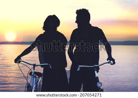 Silouette of couple carring bike on a boardwalk at sunset