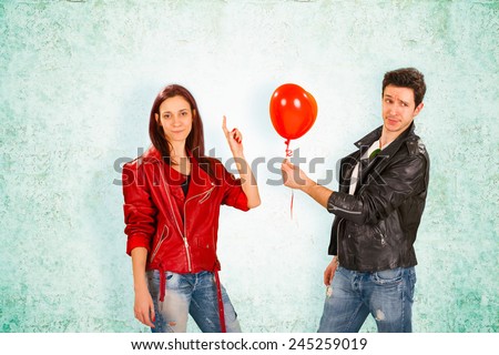 Handsome Young Man in Black Leather Jacket Offering Red Balloon to Young Woman in Red Jacket, Captured with Abstract Background.