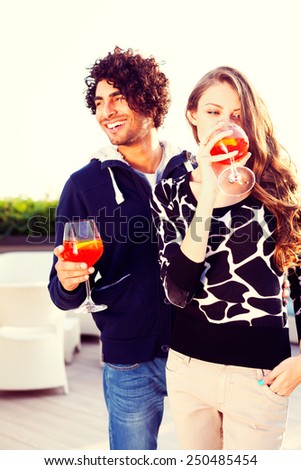 Happy vivacious couple drinking cocktails as they stand close together on an open-air patio with stylish furniture