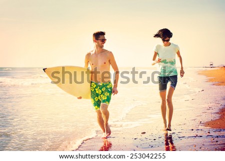 surfers couple running on the seashore at sunset