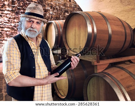 wine producer showing his bottle of wine in front of the barriques