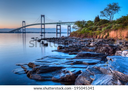 This is a long exposure HDR of the illuminated Newport bridge from Taylor\'s Point near Jamestown, Rhode Island, USA. It was taken at sunrise with a rocky seascape in the foreground.