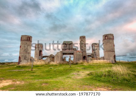 Old stone ruins of a castle, house or manor in medievel France with a dramatic grey and cloudy sky in the background and bright green grass in the foreground./ Old Stone Castle Ruins.