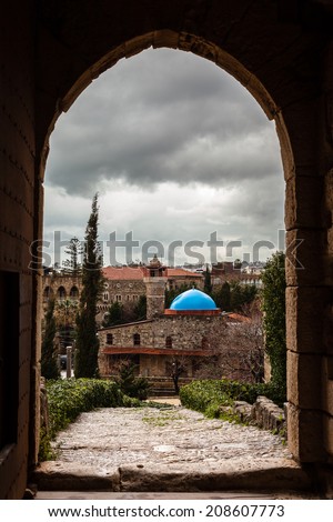 Ancient castle doorway arch in Byblos Lebanon with a blue dome mosque framed in door. Taken on grey overcast cloudy day. / Castle Gate Archway and blue Mosque.