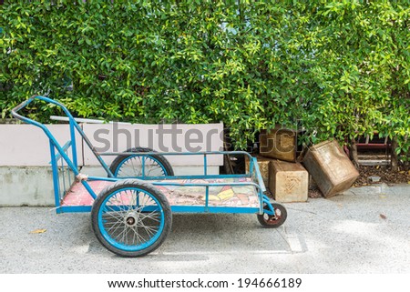 blue three-wheeled trolley on the green leaf background and old metal boxes beside