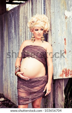 Beautiful pregnant woman with long curly blonde hair and a very large protruding belly standing wrapped in fabric holding her stomach