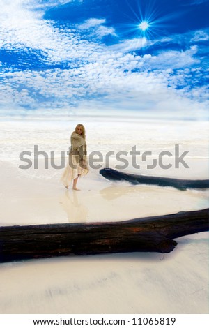Beautiful girl at the beach with a blue sky and shallow water lapping the sandy shore.