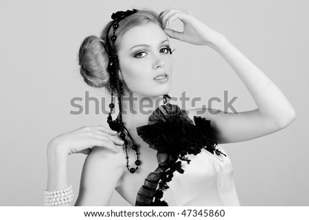 Attractive young woman wearing black feather and pearl hair dressings. She has her hand on her head. Horizontal shot.