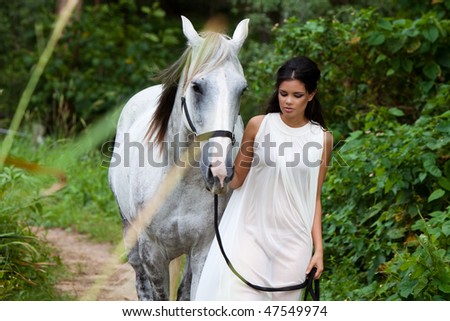 beautiful young woman leading a grey horse in the country