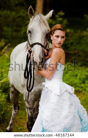 Beautiful young woman leading a grey horse in the country