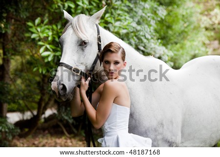 Beautiful young woman leading a grey horse in the country