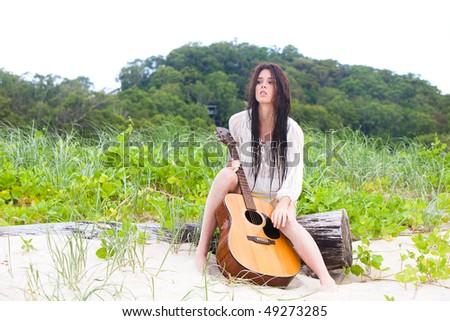 Portrait of an attractive young woman sitting on a log at the beach with a guitar.  Vertical shot.