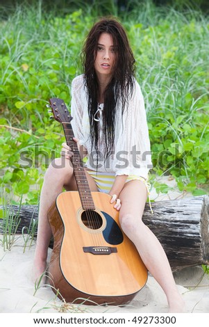 Portrait of an attractive young woman sitting on a log at the beach with a guitar.  Vertical shot.