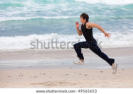 Full length profile view of a young man running in the surf on the beach. Horizontal shot.