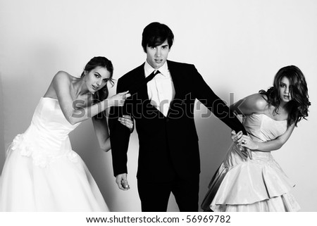 Two attractive young women wearing formal attire are pulling a young man in a suit between them. Horizontal shot.