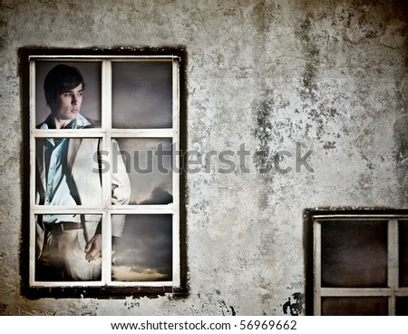 Handsome young man is standing behind a window with a stormy sky in the background. Horizontal shot.