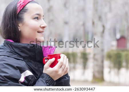 Beautiful woman holding a red mug with coffee wearing mountain cloth