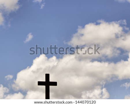 A black cross with blue sky and white clouds as background