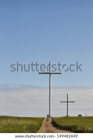 A narrow gravel road leading up to two crosses against a blue and white sky
