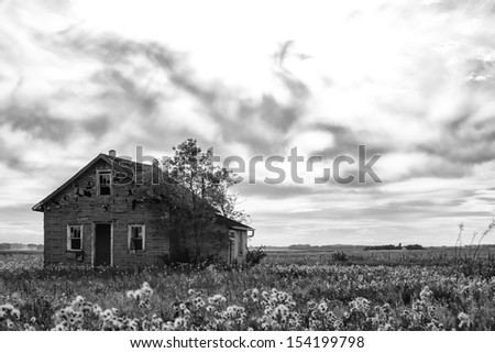 A black and white photo of a small old house with wispy clouds