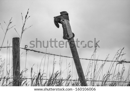 A black and white photo of a cowboy boot upside down on a fence post
