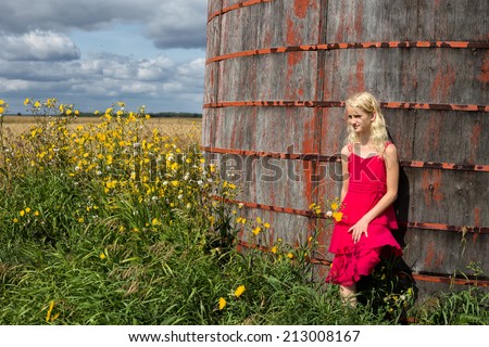 Young girl in,pink dress leaning against grain bin