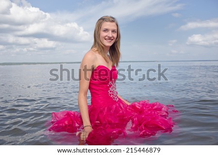 Girl in red prom dress standing in lake